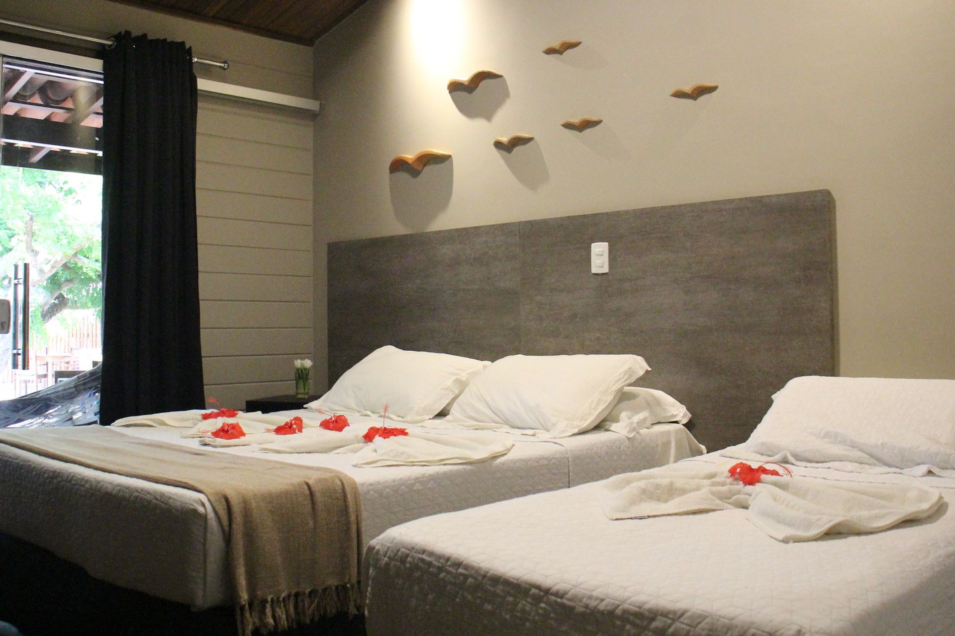 Um quarto com duas camas e uma janela com pássaros na parede.