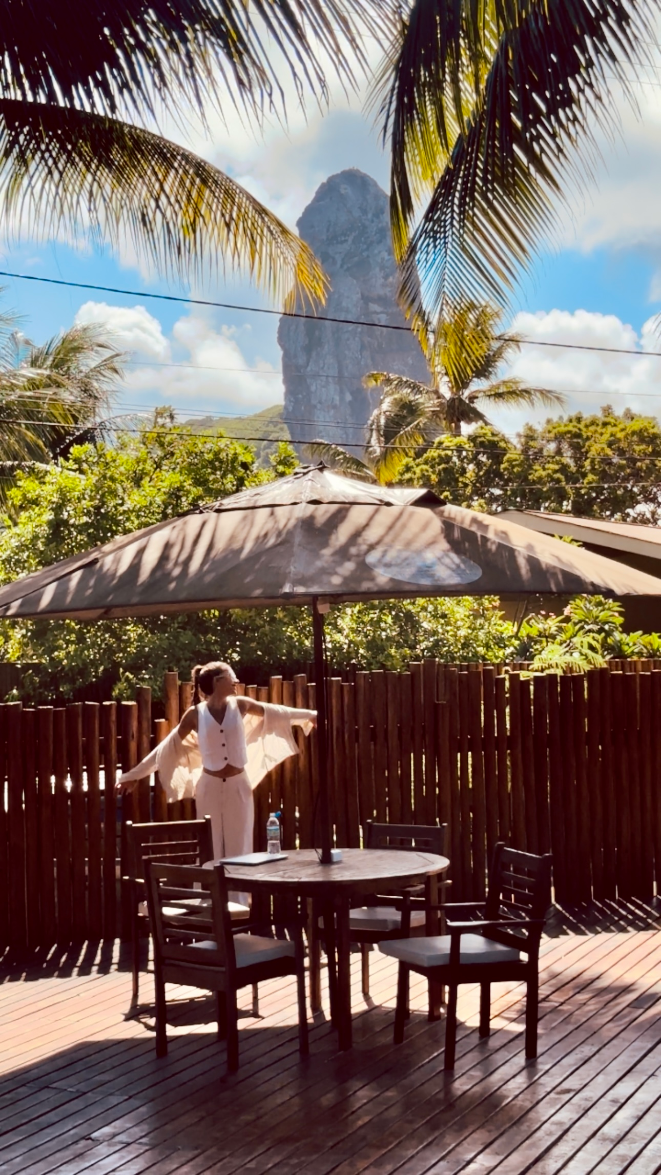 Uma mulher está parada em frente a uma mesa e cadeiras sob um guarda-chuva.