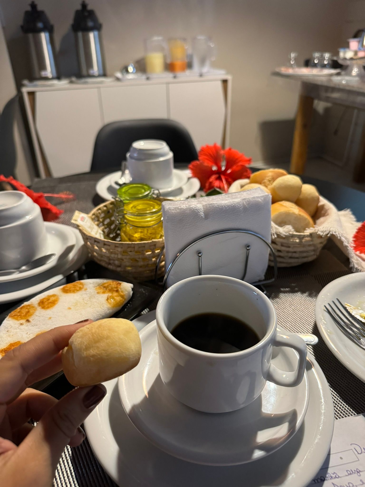 Uma pessoa está segurando um pedaço de pão ao lado de uma xícara de café.