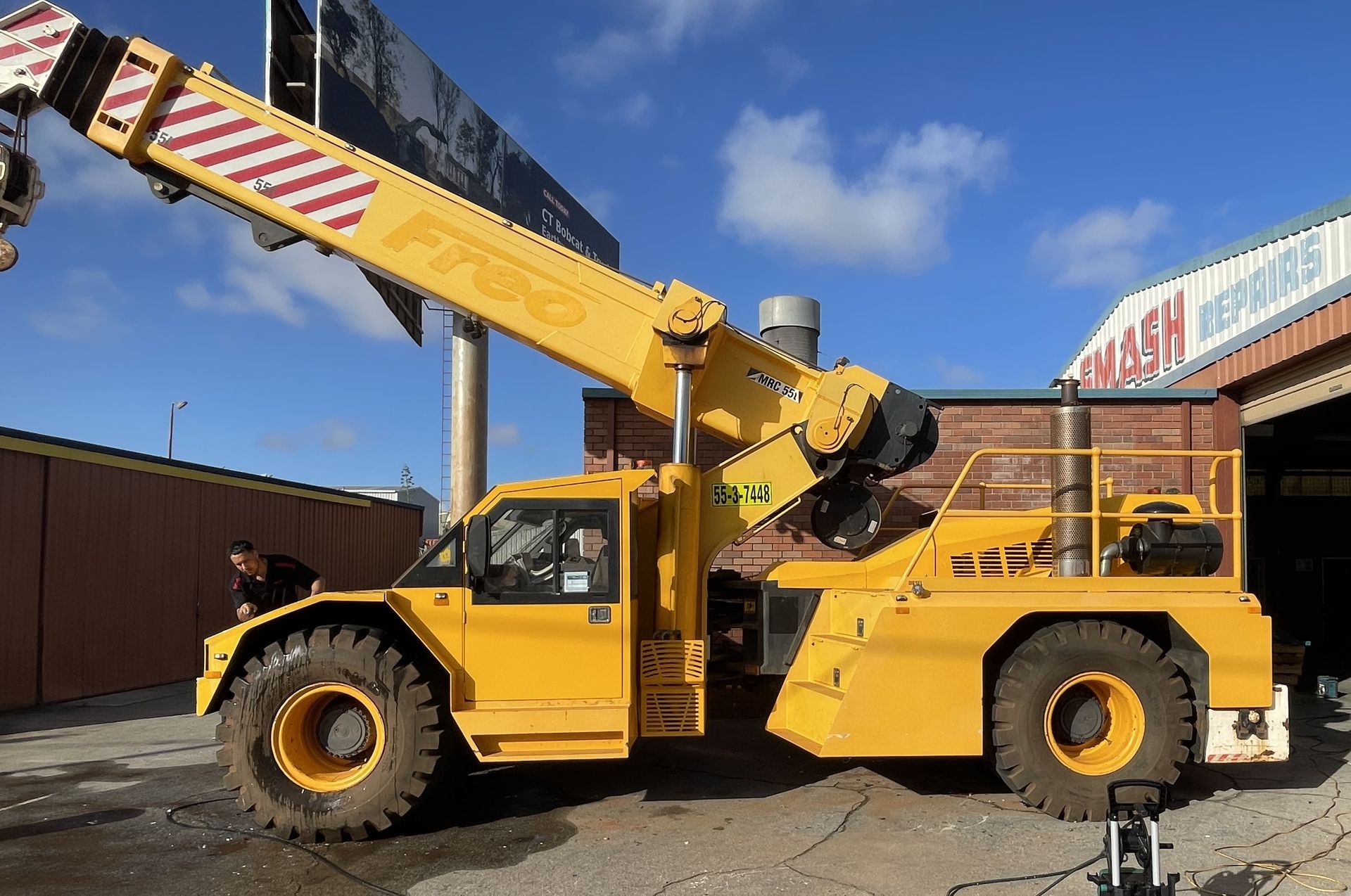 Yellow crane truck with extended boom parked outdoors under a blue sky