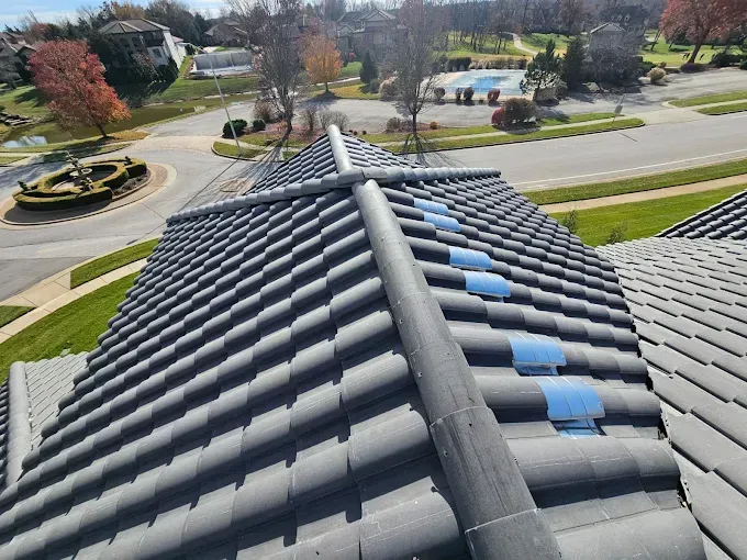 Overhead view of a dark gray tiled roof with a pipe running along the top, with blue tape.