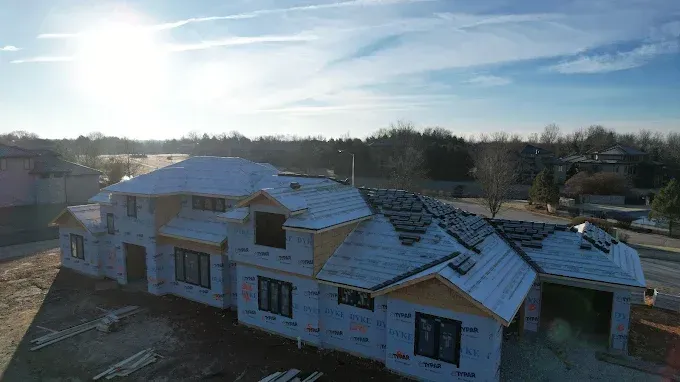 House under construction, exterior view, with partially installed roof and siding on a sunny day.