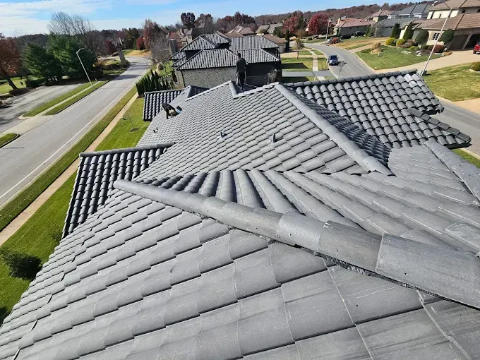 Gray tile roof of a house with a street and houses in the background. Sunny day.