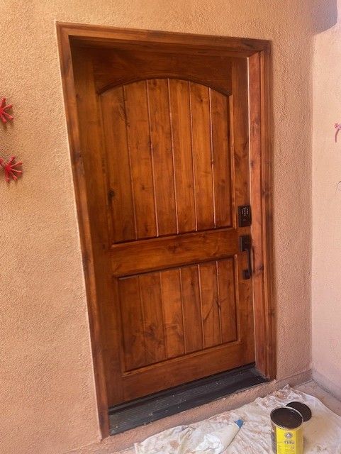 Wooden front door with arched top and dark hardware set in a light brown exterior wall.