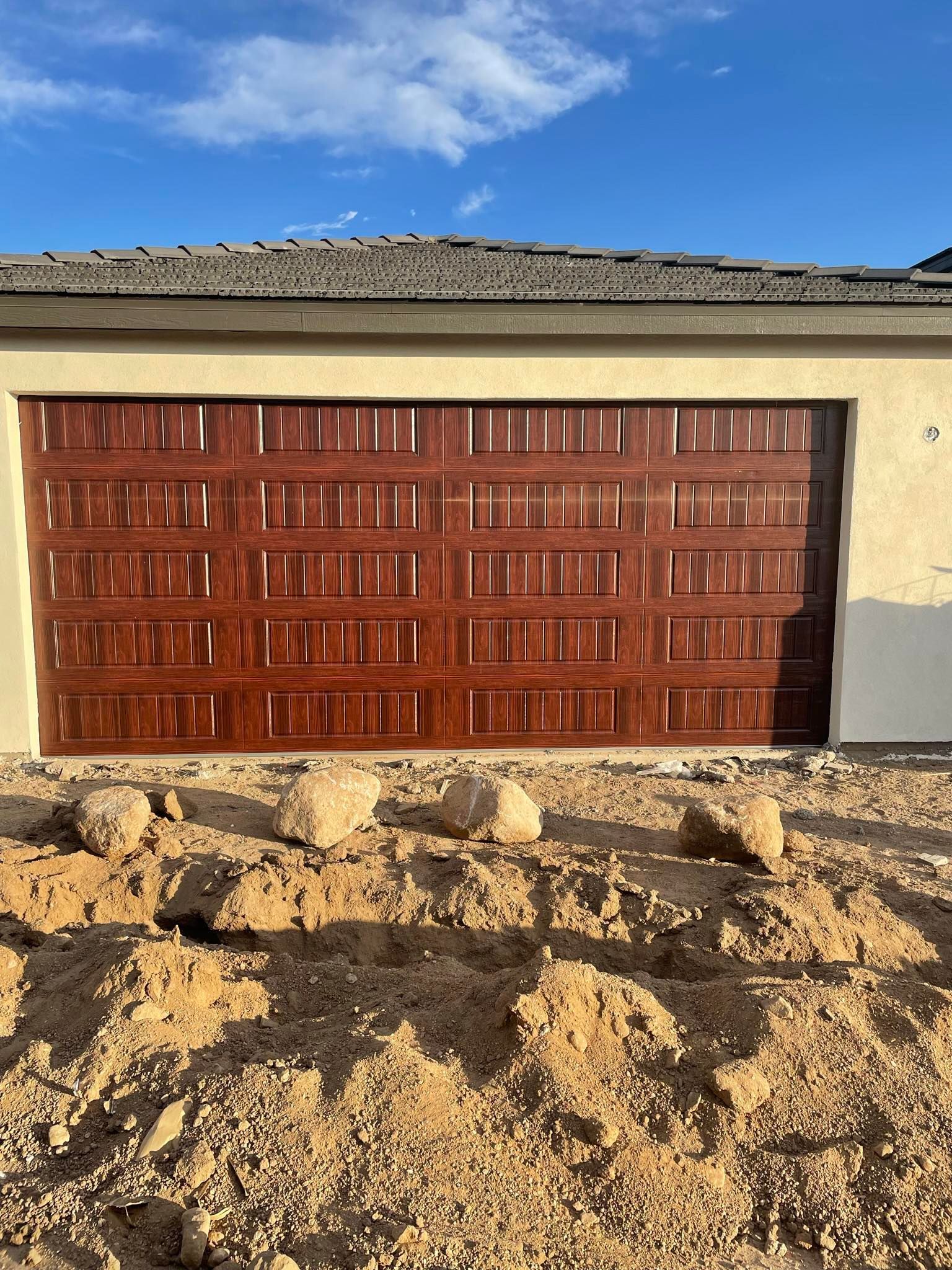 Garage door reflecting a truck and trees on a sunny day. Black frame, concrete base, and gravel ground.