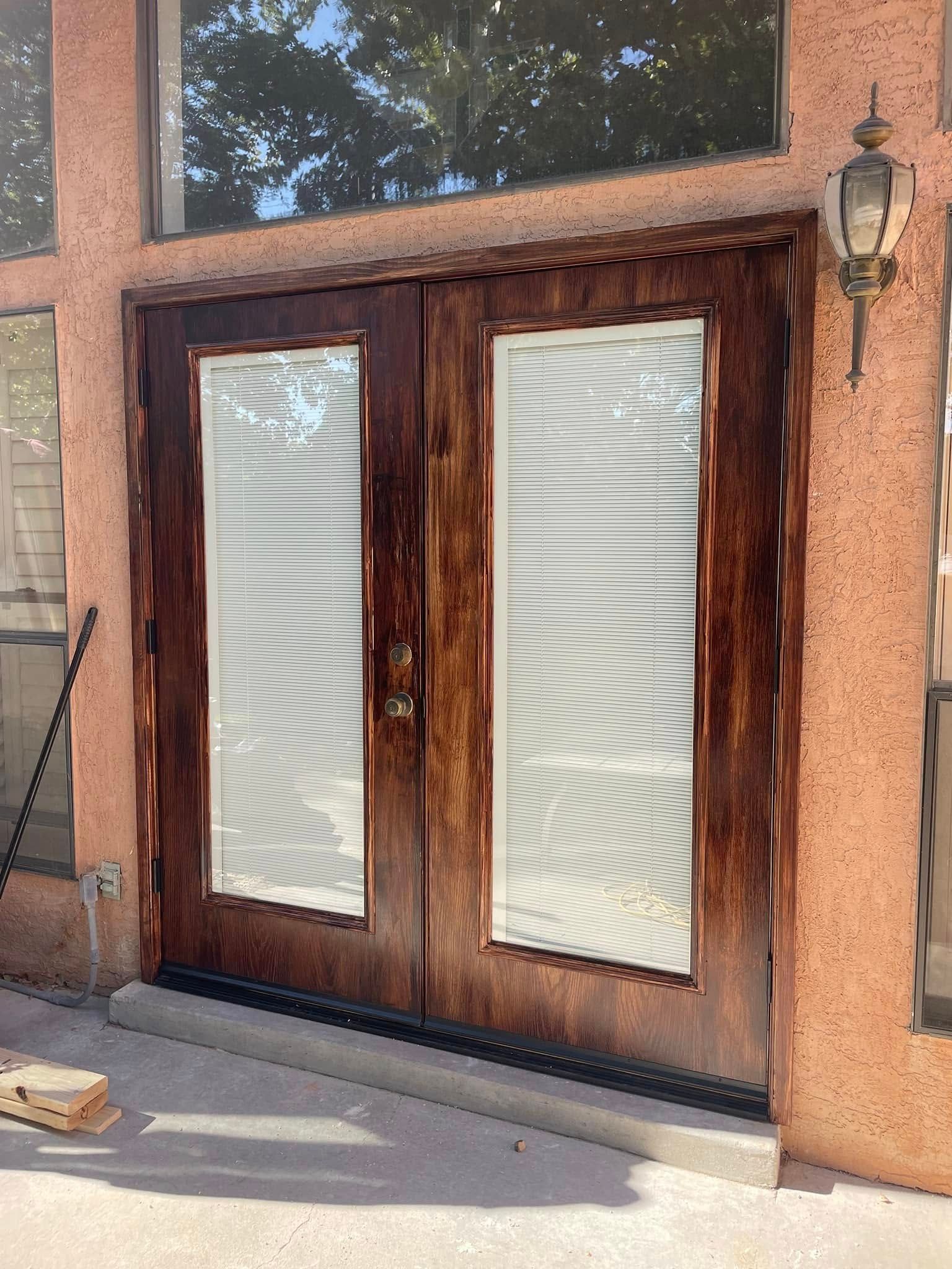 Dark wood double doors with glass panels and white blinds, set in a peach-colored stucco wall.