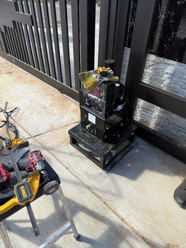 Black automatic gate motor on concrete next to a dark metal gate.