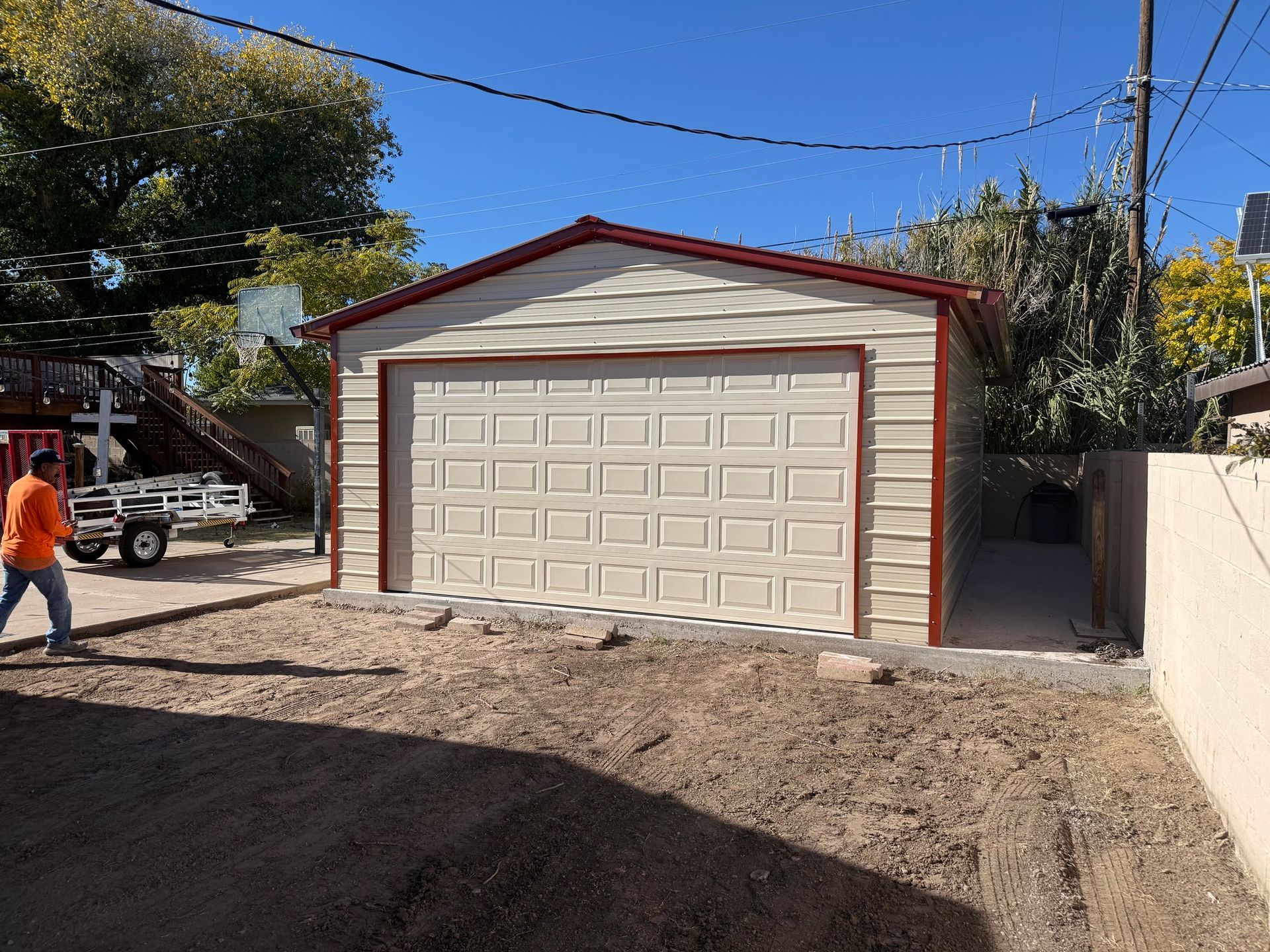 Tan metal garage with a red trim and a concrete driveway. A person walks near the garage.