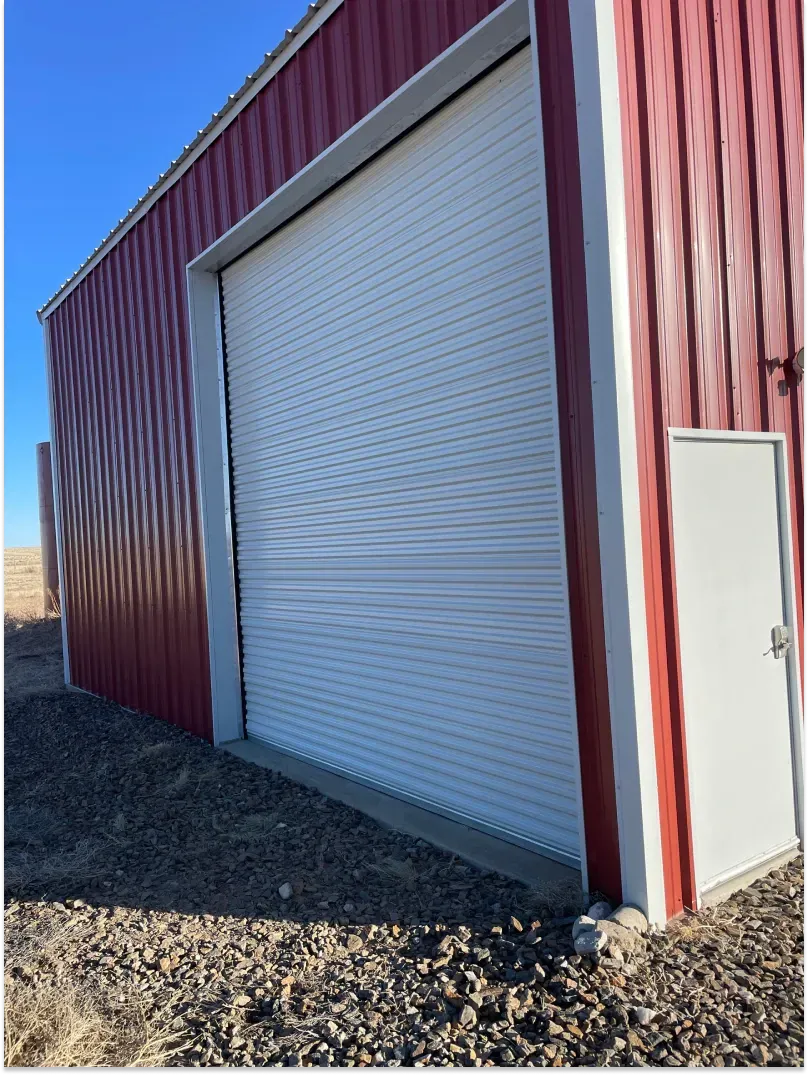 Red metal building with white roll-up door and small side door, blue sky background.