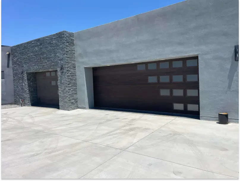 Two garage doors: one gray stone, one brown with gray concrete structure under a clear blue sky.