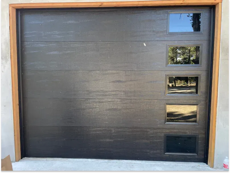 Black garage door with horizontal texture, four square windows, wooden trim.