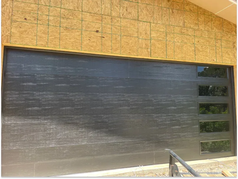 Black modern garage door with four windows, installed in a building under construction.