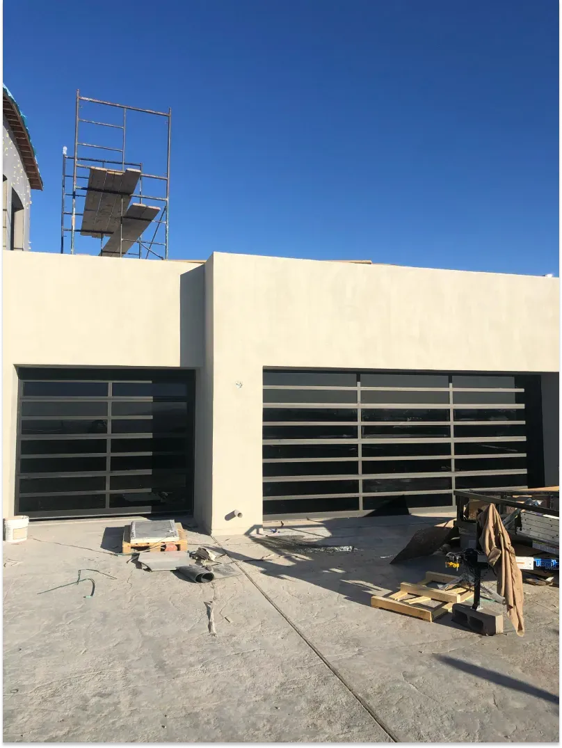 Two black-framed garage doors with horizontal glass panels. Construction site with a blue sky.