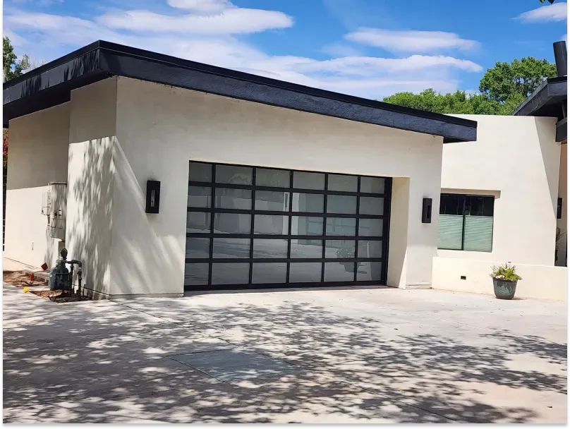 Modern white building with glass garage door, black trim, and blue sky.
