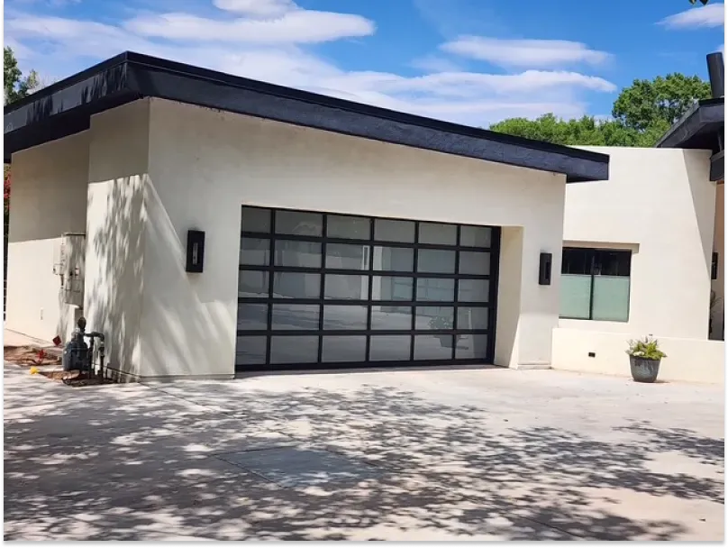 Modern garage with glass door and black trim. Cream stucco exterior, blue sky.