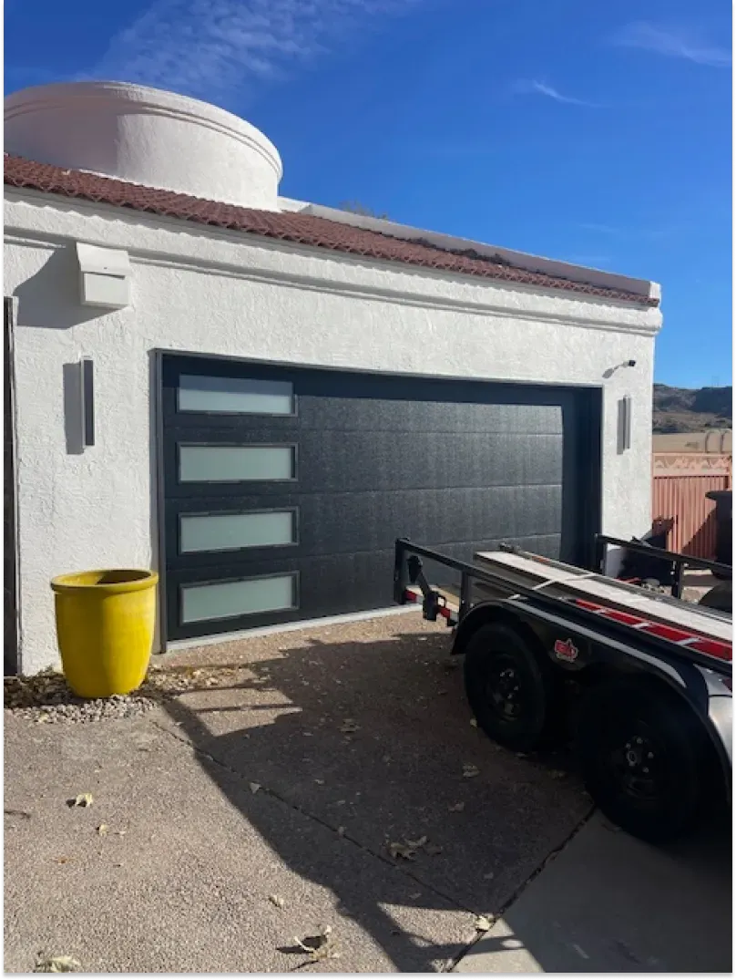 Black garage door with frosted windows, next to a yellow planter, and trailer.