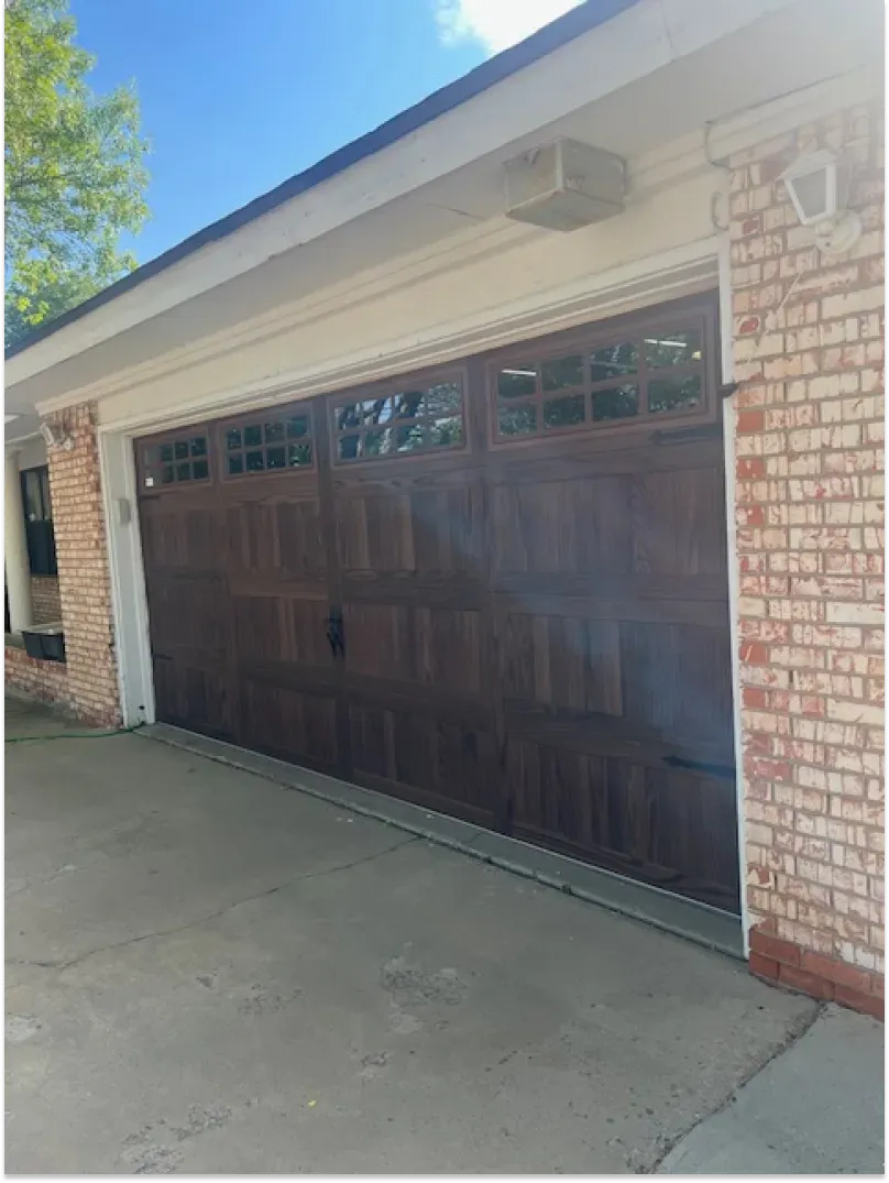 Brown garage door with windows, flanked by brick, under a white soffit. Concrete driveway.