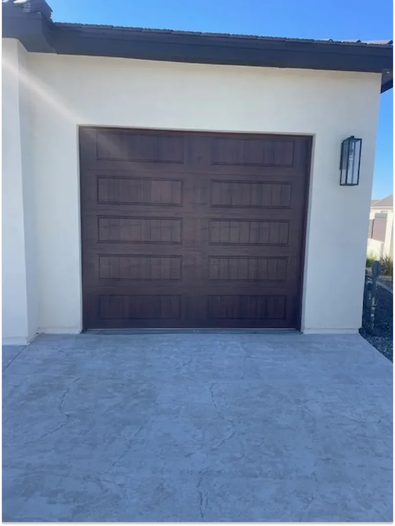 Brown garage door on a light-colored stucco building with a concrete driveway.