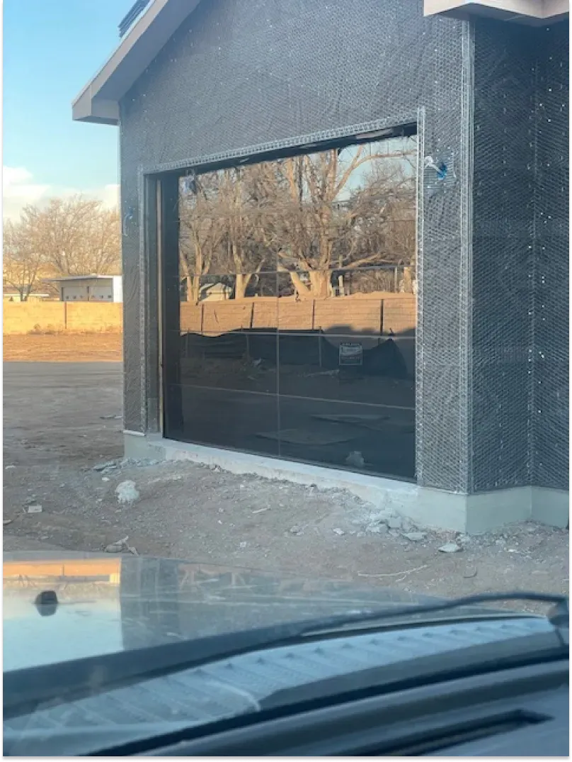 Garage under construction with a large glass door reflecting trees and sky.