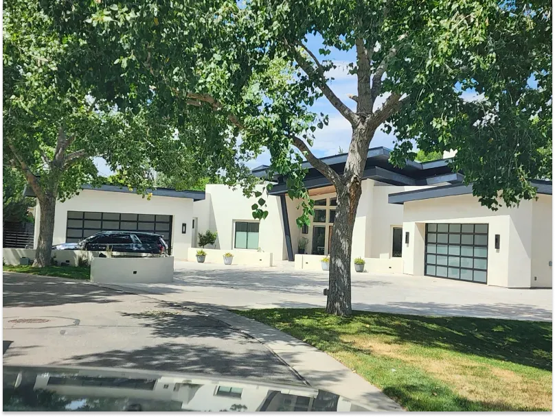 Modern white house with glass garage doors, large trees, and a circular driveway.