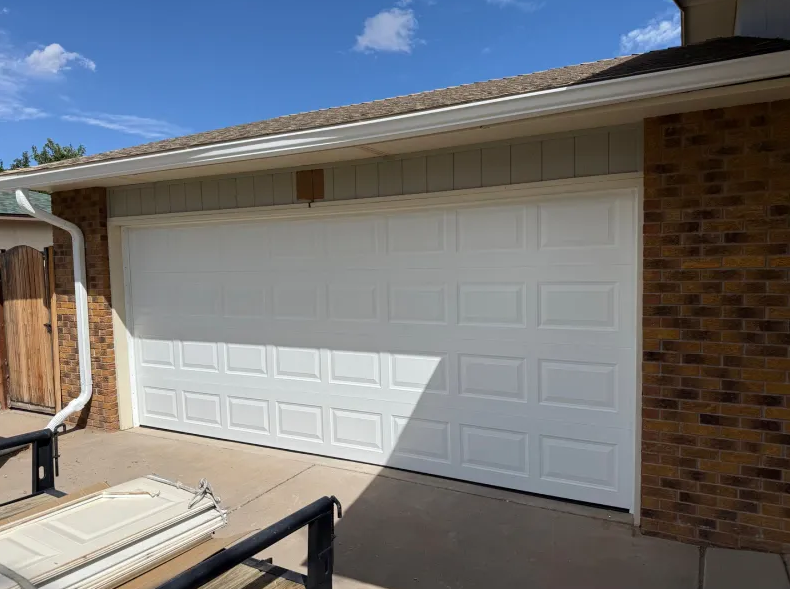 Beige house with a white garage door; a trailer is parked in front.