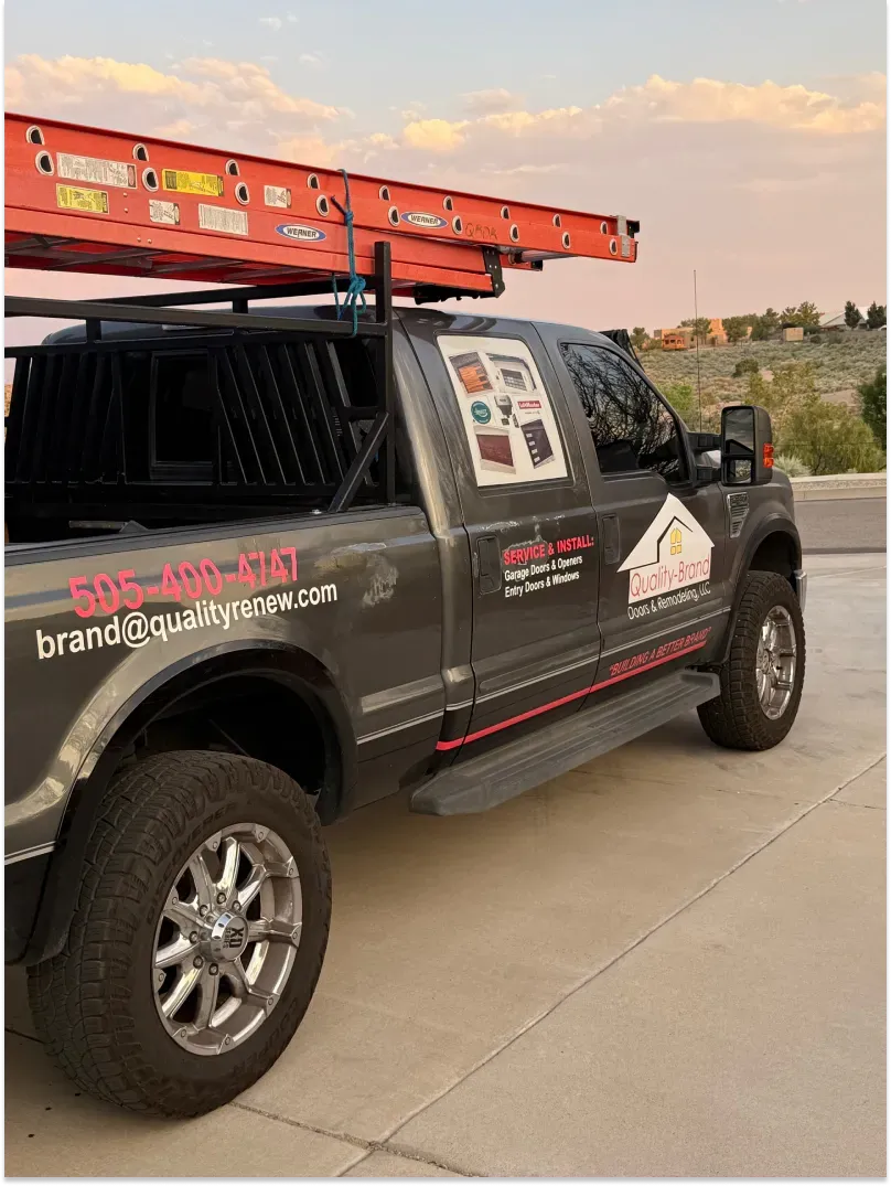 Gray work truck with ladder on top, parked in driveway. Logo on door, dusk setting.
