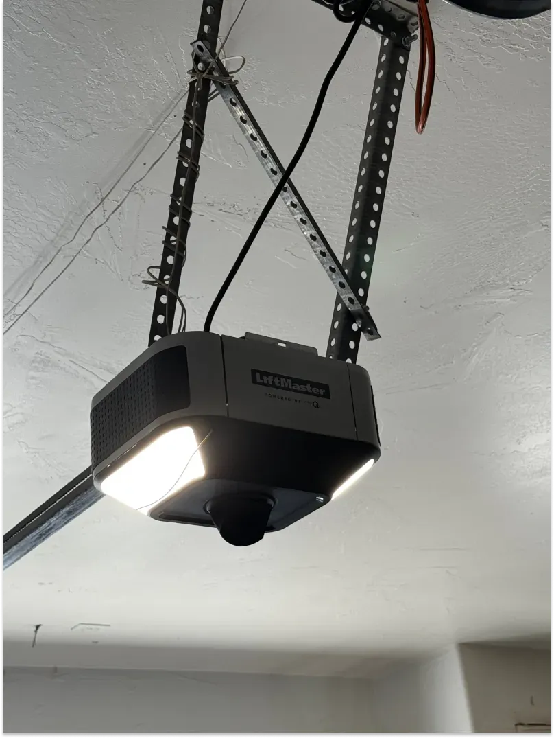Garage door opener unit mounted on a ceiling with a bright LED light.