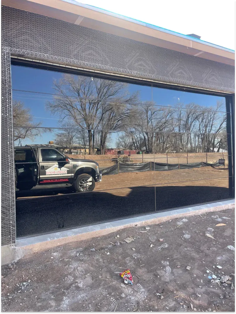 Reflective black garage door showing a pickup truck, trees, and sky.