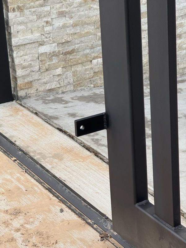 Black metal gate and attached bracket against a stone wall.