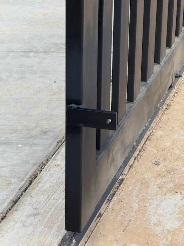 Black metal fence section on concrete, showing a bracket where the gate would open.