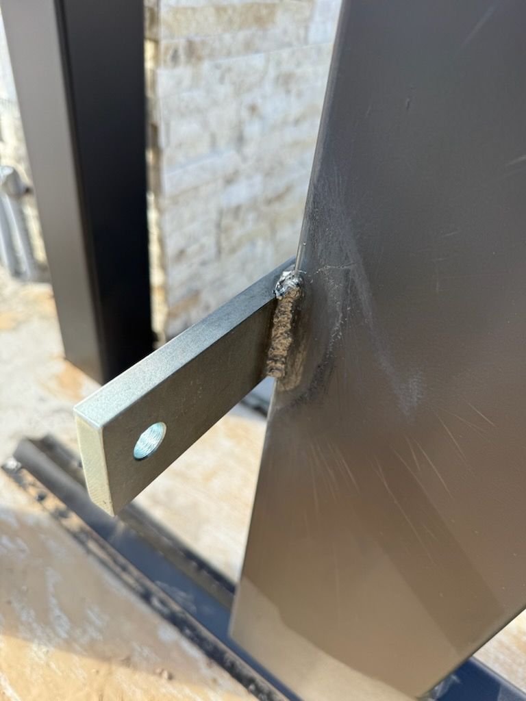 Gray metal bracket welded to a larger gray metal structure. A hole is in the end of the bracket.