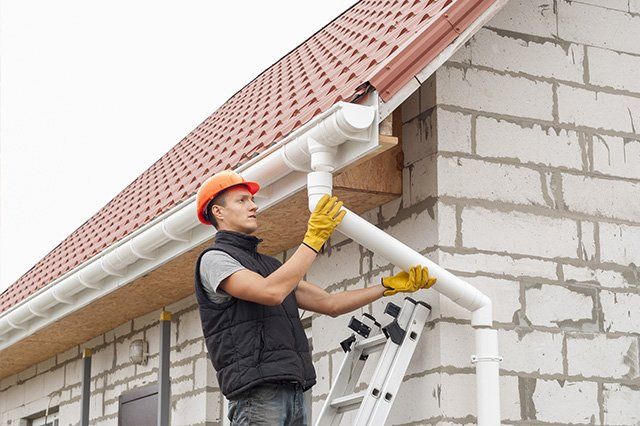 Professional installer working on a gutter system, carefully securing and aligning the gutters along the roofline to ensure proper water drainage and protection for the house.