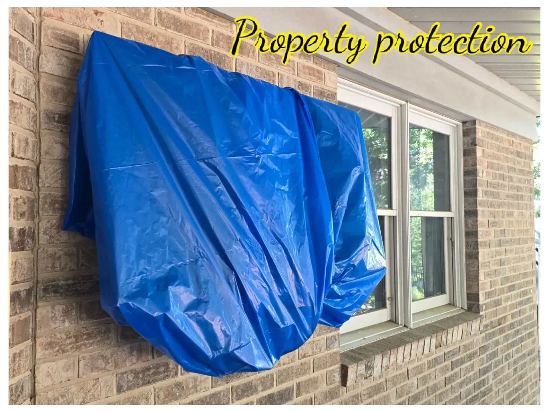 A blue tarp is covering a window on a brick wall.