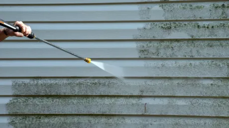 A person is cleaning a house siding with a high pressure washer.