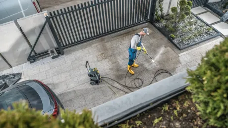 A man is using a high pressure washer to clean a driveway.