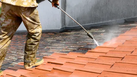 A man is using a high pressure washer to clean a brick walkway.