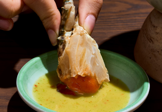 A person is dipping a crab in a bowl of sauce.