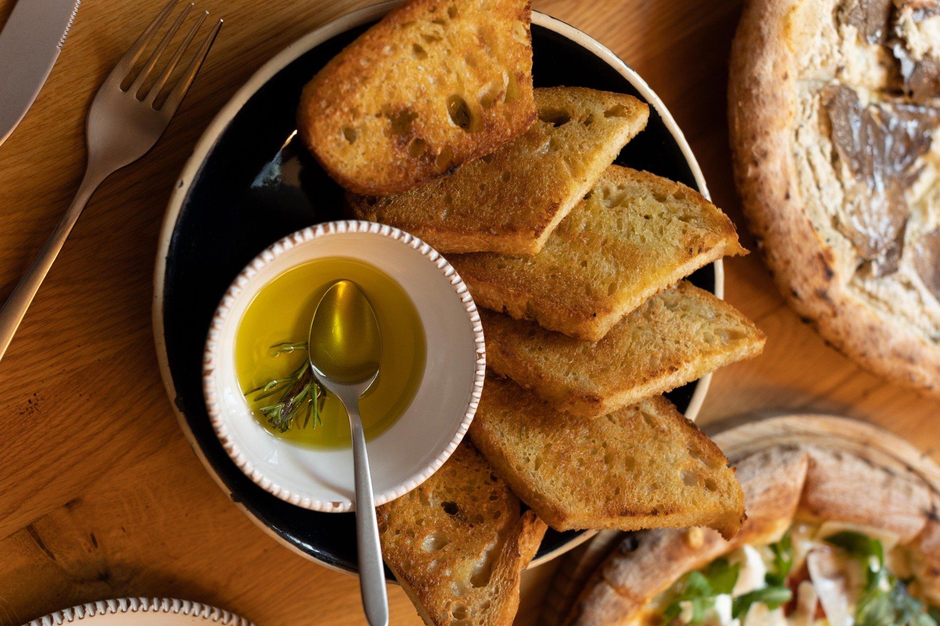 Une assiette de pain avec un bol d'huile d'olive et une cuillère sur une table.