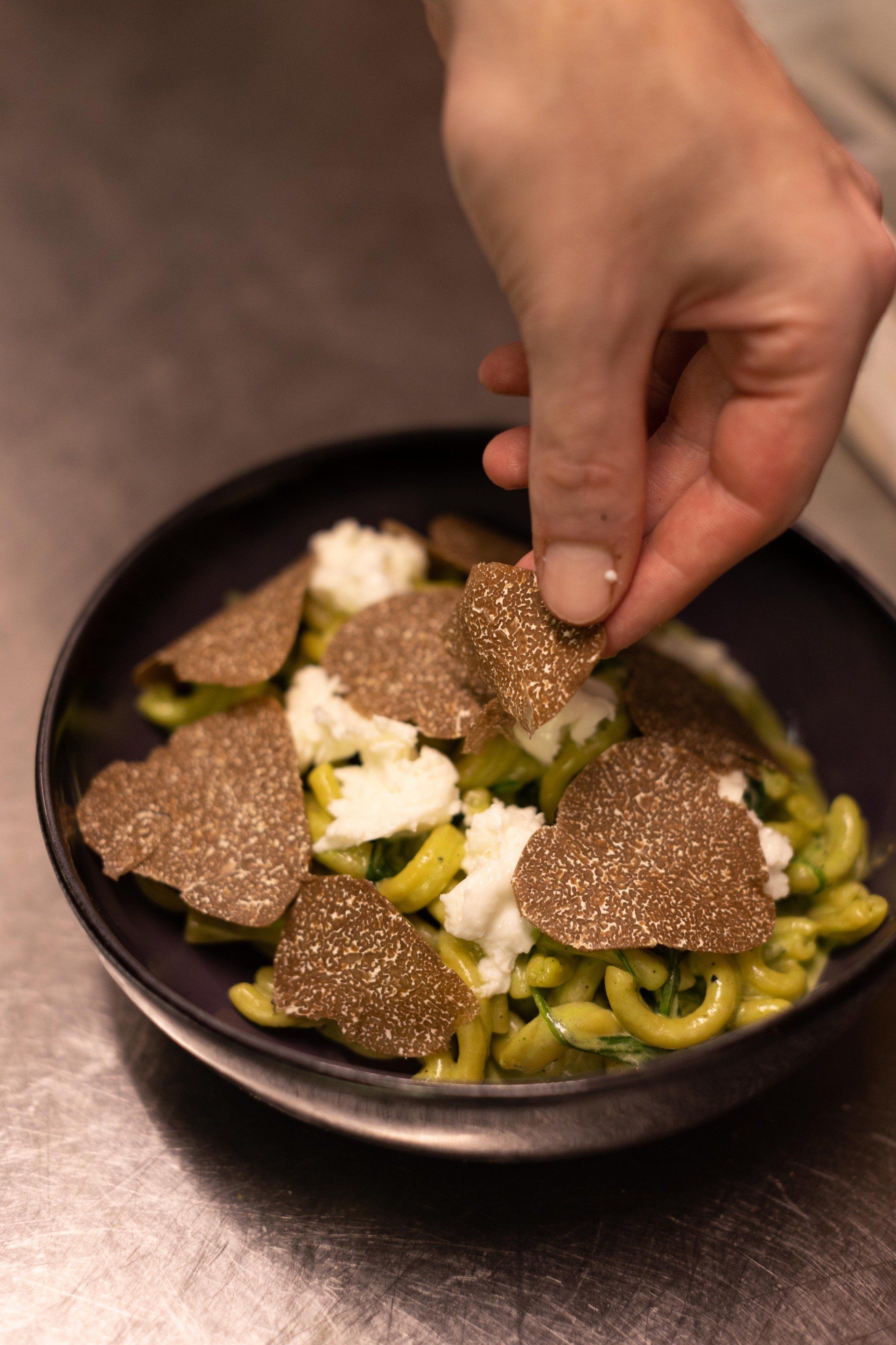Une personne ajoute de la truffe à un bol de pâtes.
