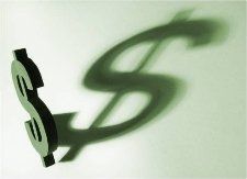 A dark dollar sign casting a large, blurred shadow on a light green surface.