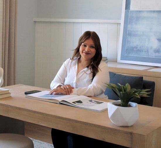 A woman is sitting at a desk with a laptop and a vase of flowers.