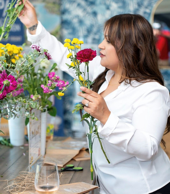 A woman is sitting at a desk with a laptop and a vase of flowers.