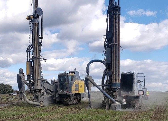 two drill rigs are working in a field on a cloudy day .