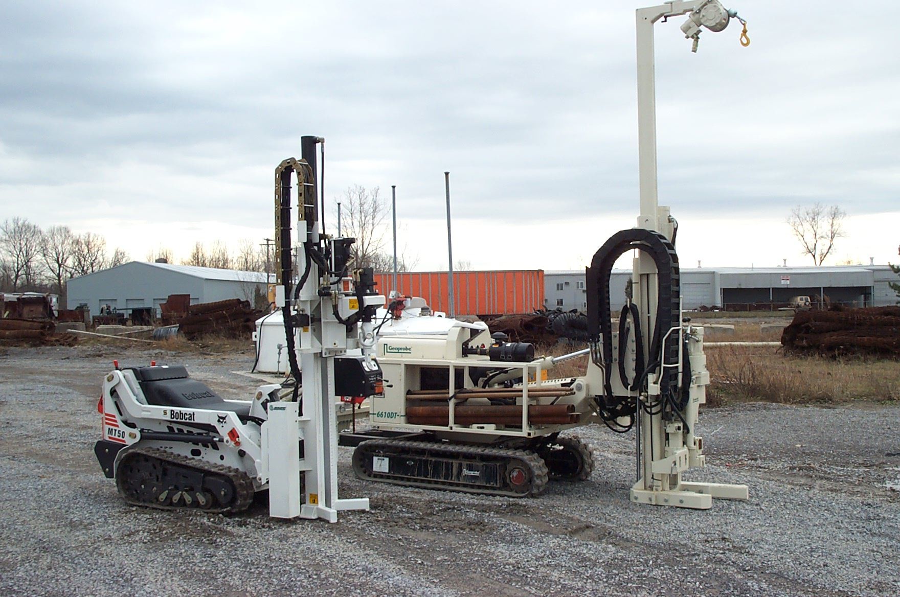 two drill rigs are parked in a gravel lot
