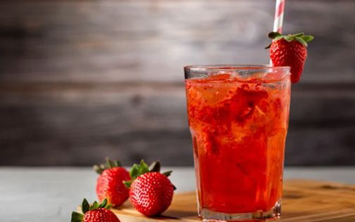 Strawberry cocktail in a tall glass, garnished with a strawberry, on a wooden board.