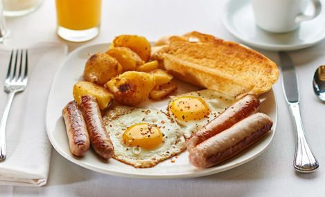 Plate of fried eggs, sausage, potatoes, and toast; orange juice and coffee in the background.