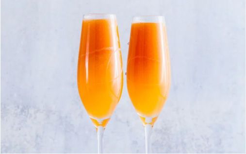 Two fluted glasses filled with orange liquid against a white background.