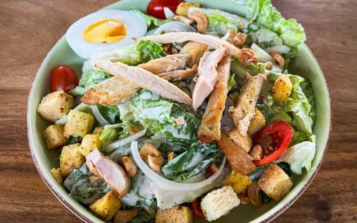 Salad with chicken, egg, tomatoes, croutons, and cashews in a green bowl.