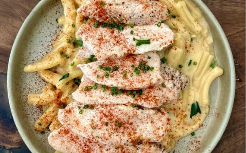Sliced chicken with paprika and chives atop mashed potatoes and fries on a plate.
