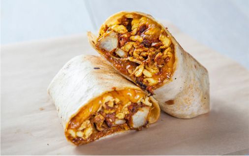 Breakfast burrito cut in half, showcasing eggs, potatoes, and sauce filling wrapped in a flour tortilla.